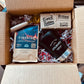 Open cardboard box containing a coffee package, chocolate bar, and other items.