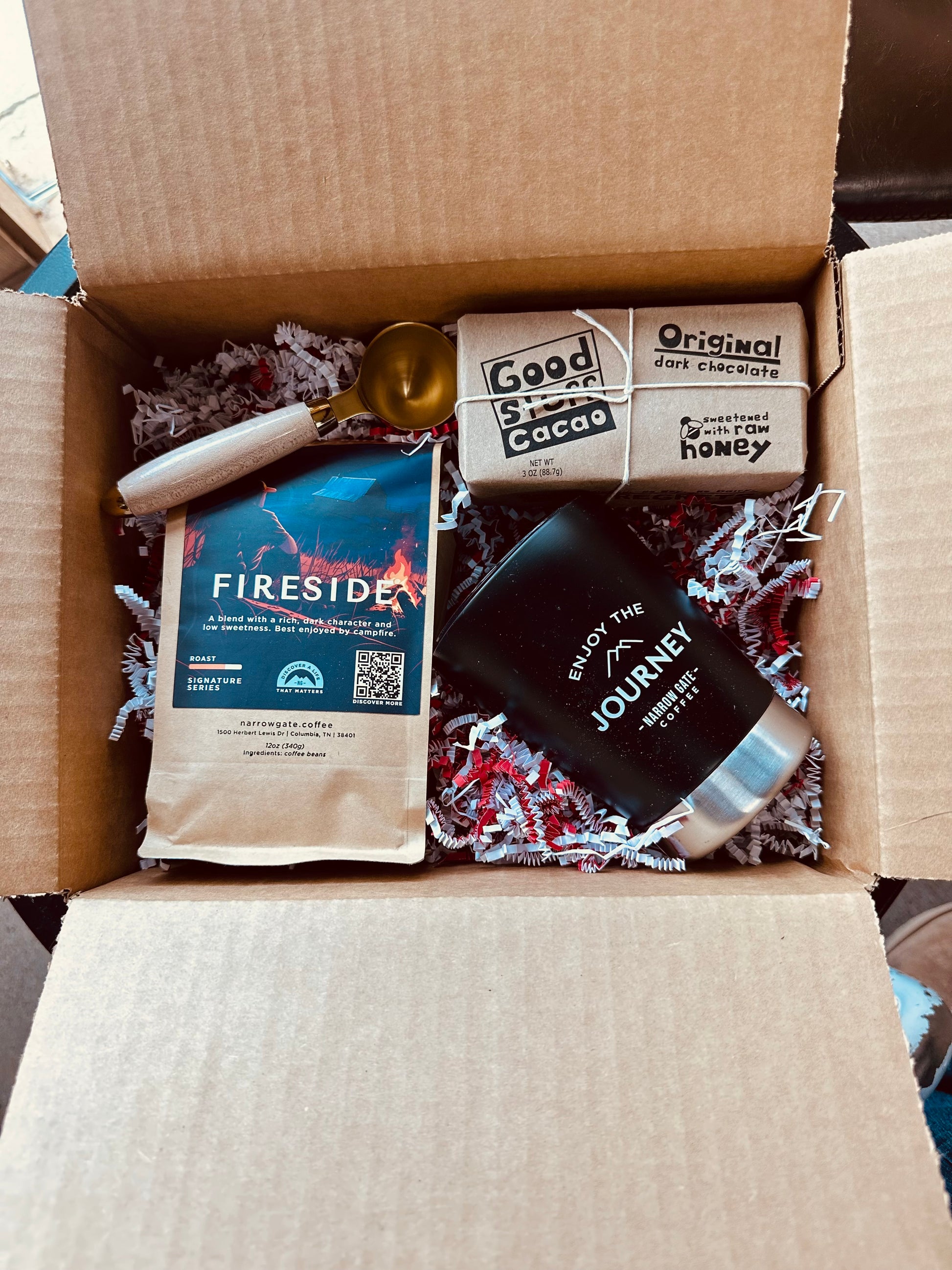 Open cardboard box containing a coffee package, chocolate bar, and other items.